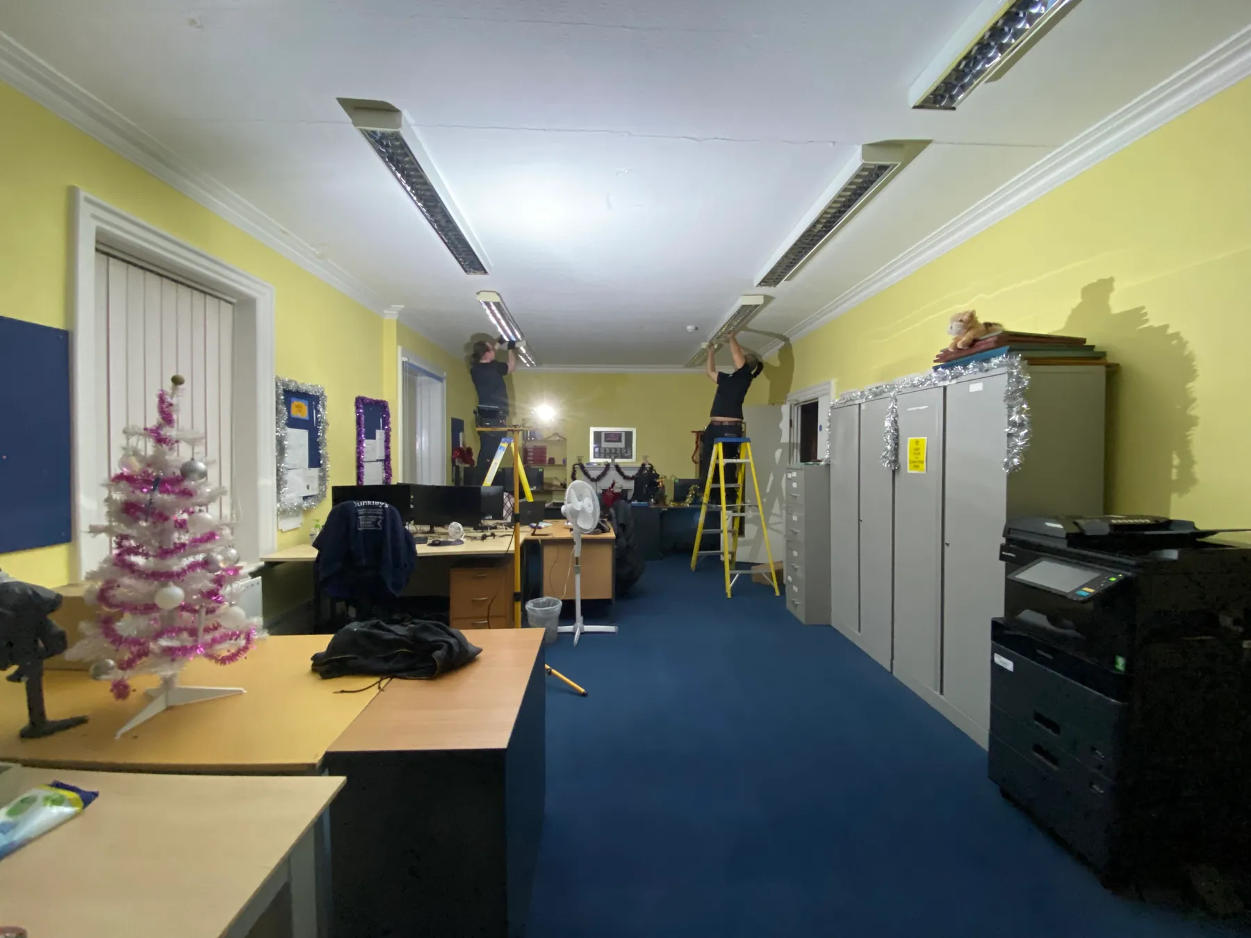 Electricians working on ceiling lighting in an open-plan office